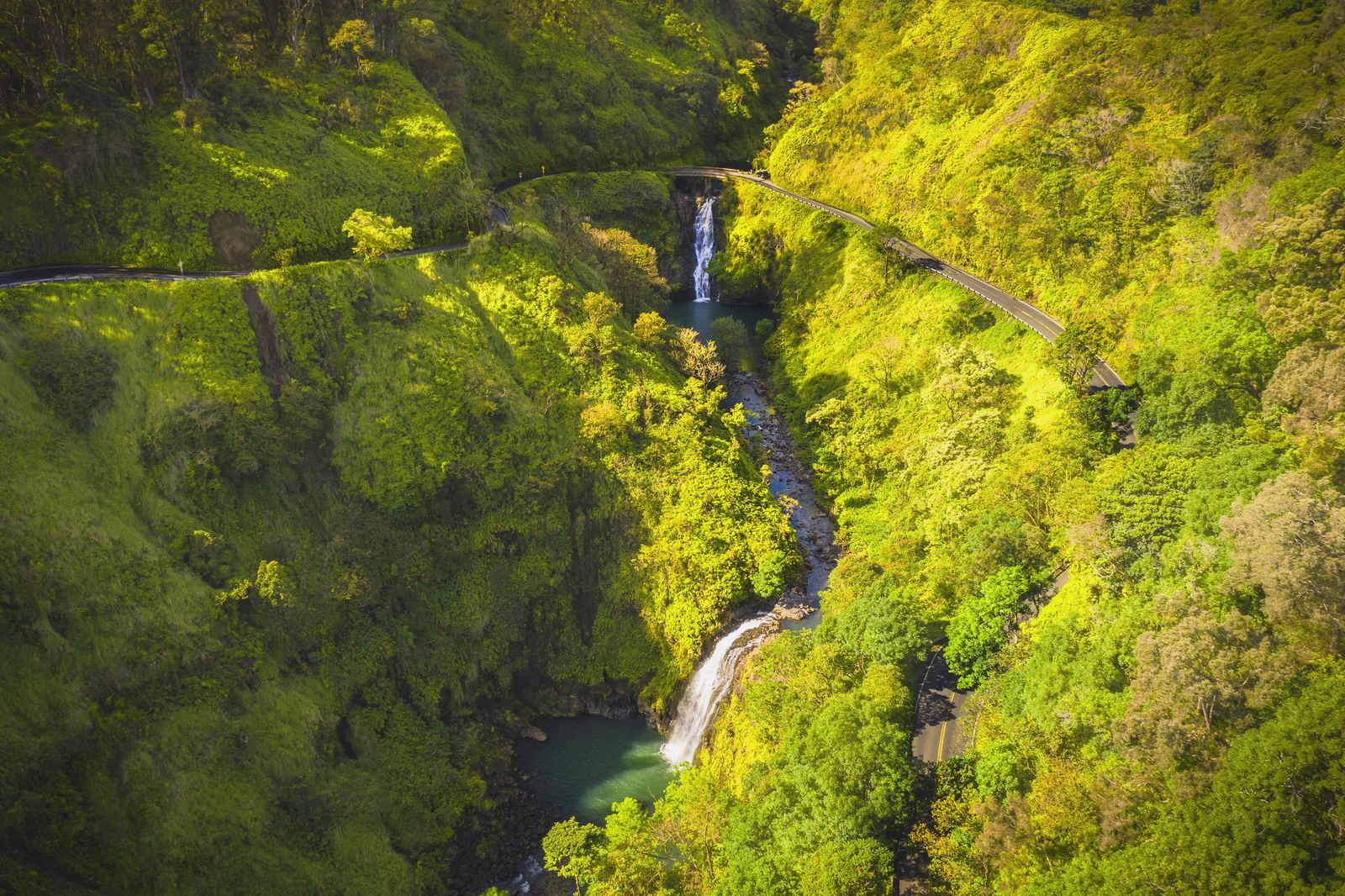 Aerial view of a waterfall running through a green Maui valley