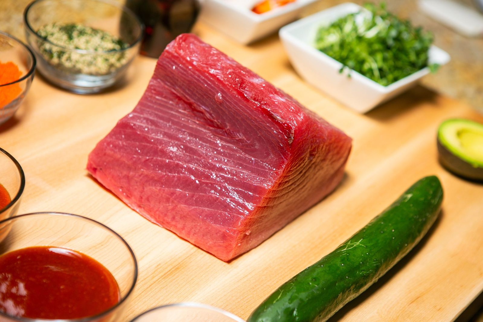 A block of raw ahi on a board with vegetables and sauces