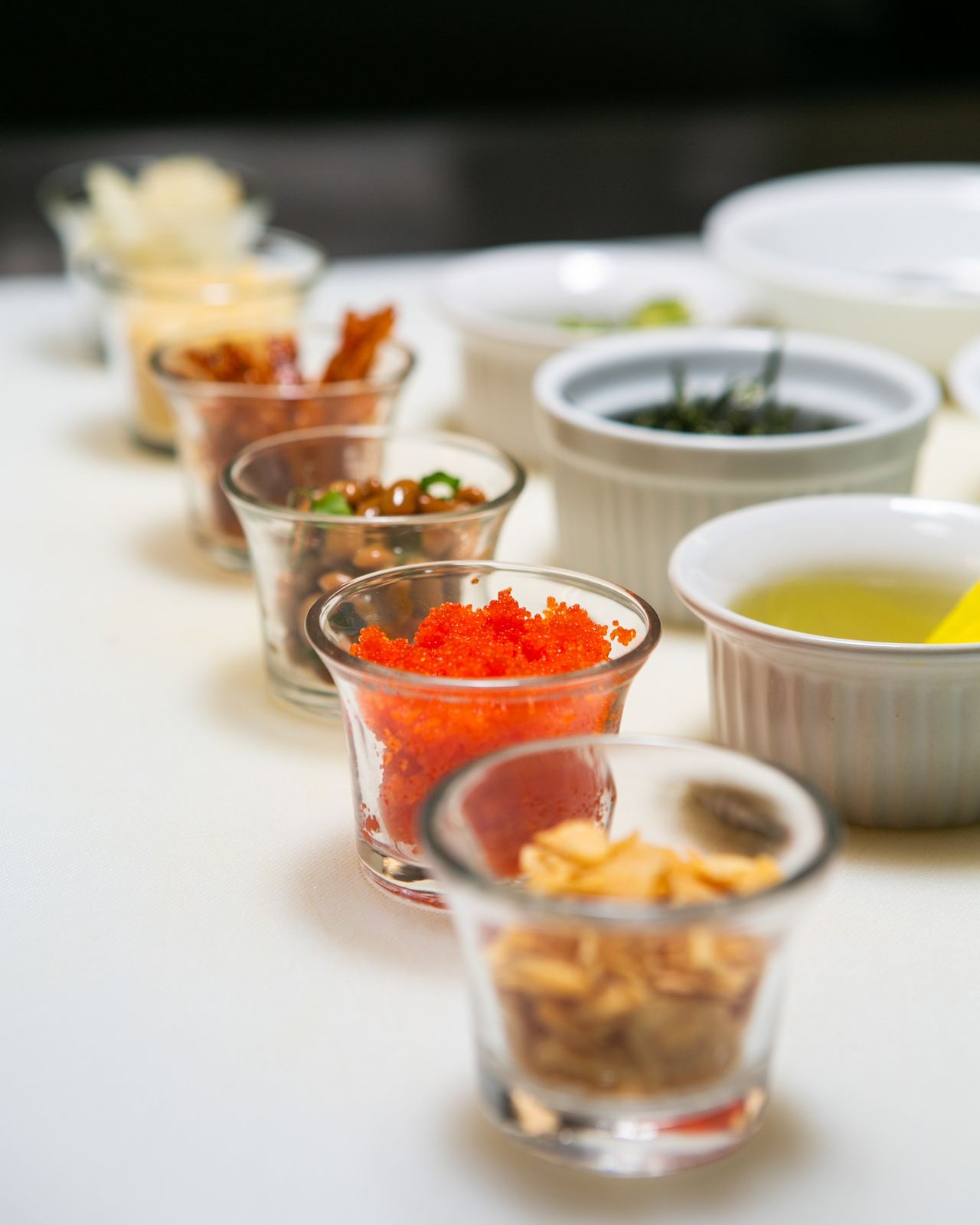 Small bowls of poke toppings and sauces on white