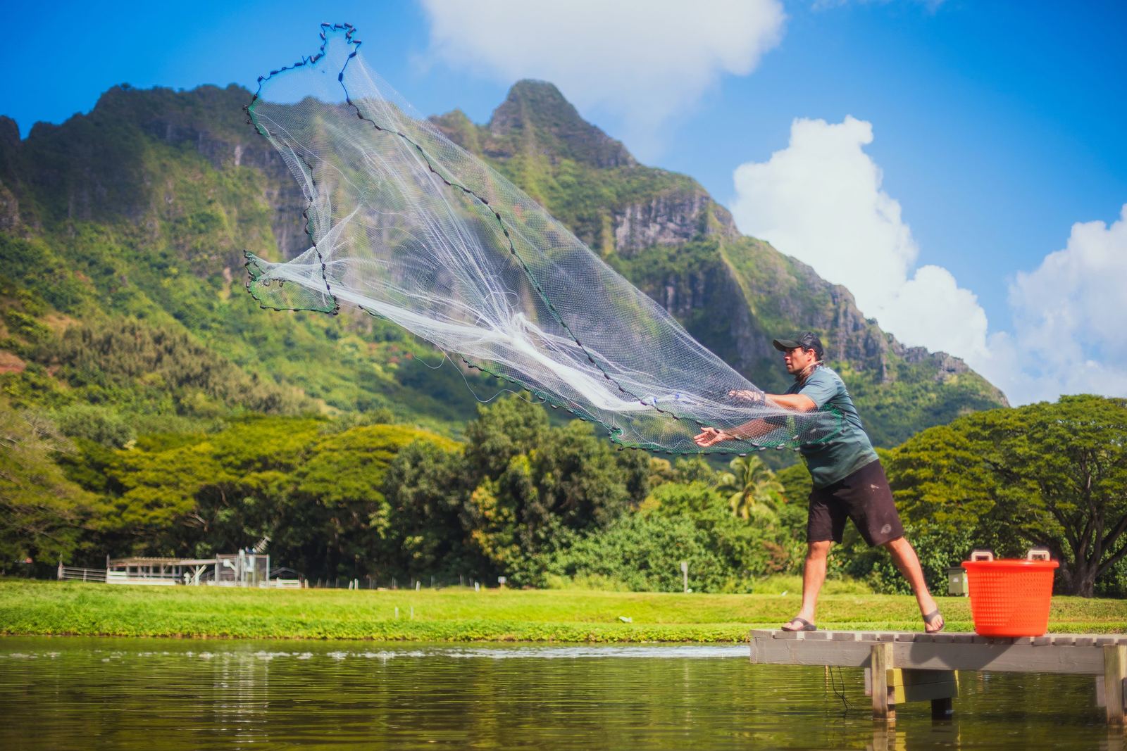 A worker beside a reservoir with the Kualoa mountains behind
