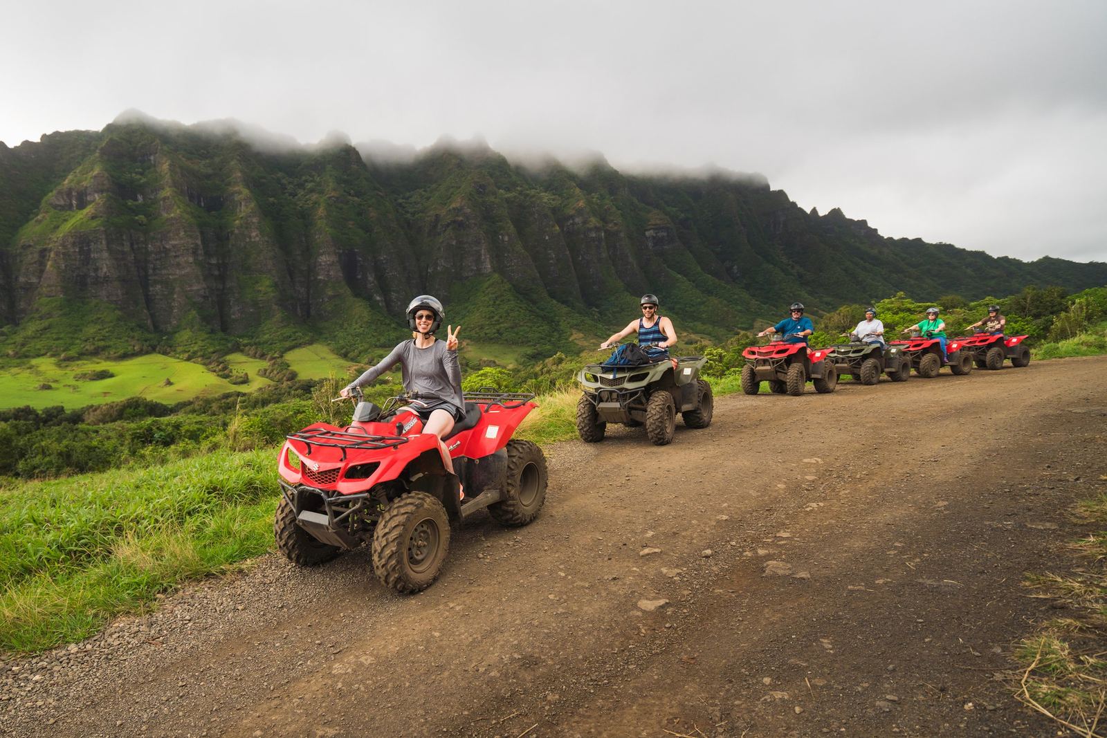 Riders on ATVs on a dirt road below the Kualoa ridge