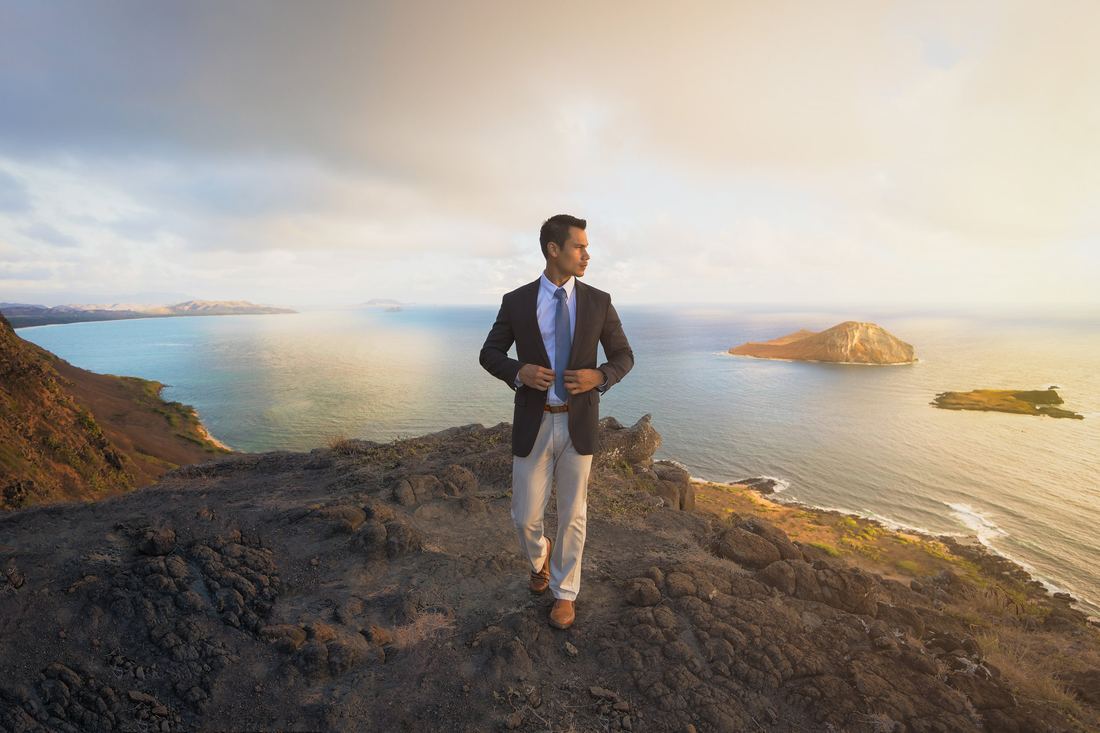 A man in a suit standing on a cliff edge at sunrise