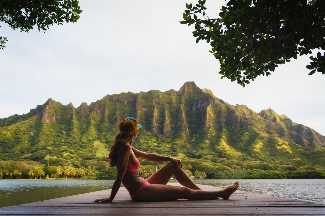 A woman seated by a lagoon below the Kualoa ridge