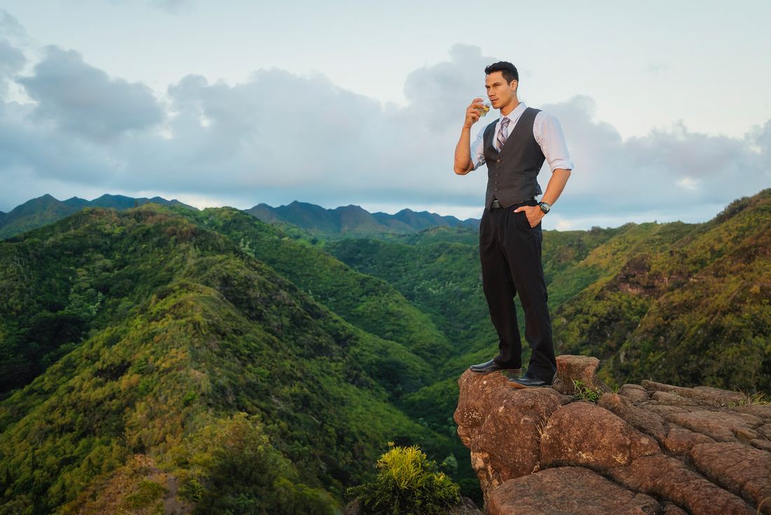 A man in formal dress on a rock outcrop above the valley