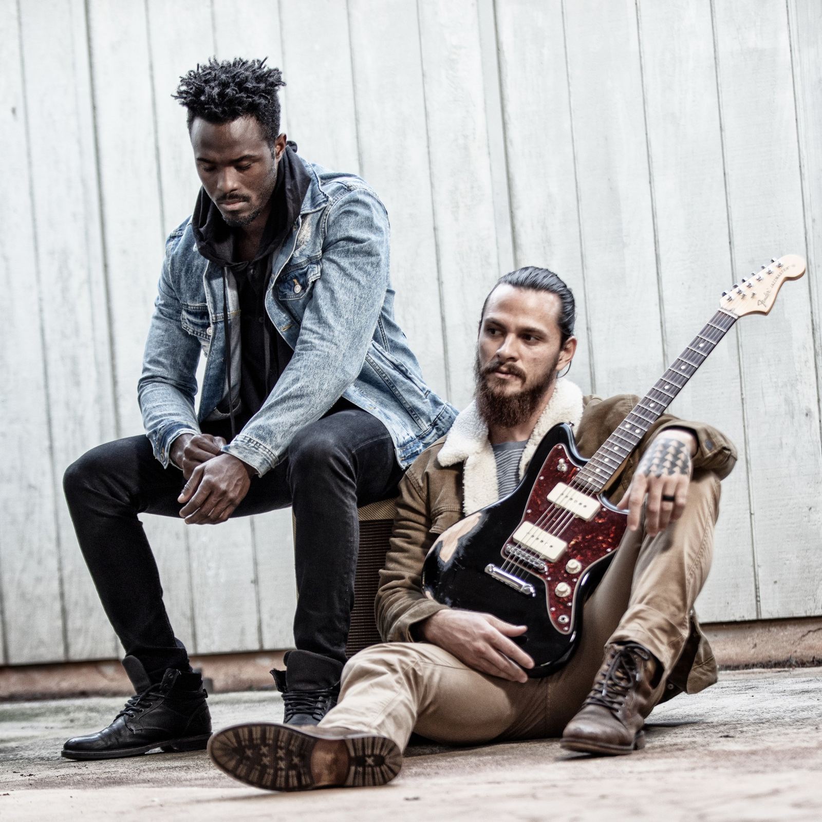 Two musicians seated against a wall with a guitar
